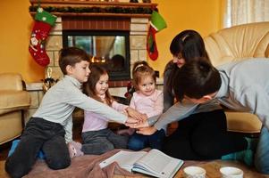 Happy young large family at home by a fireplace in warm living room on winter day. photo