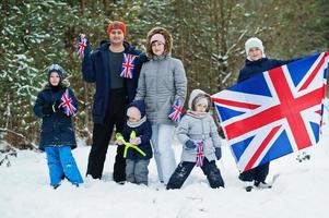 Family with four kids holding flag of Great Britain on winter landscape.