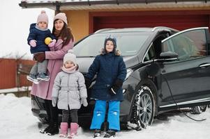 Young mother with kids charging electric car in the yard of her house at winter. photo