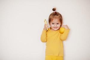 Baby girl in yellow with lemon and mobile phone, isolated background. photo