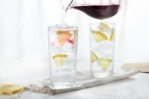 Two glasses of ice cold lemonade on linen napkin on white background in blur. photo