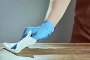 A man's hand in medical glove wipes the table with napkin. Background waiter in an apron in blur. Surface treatment. photo