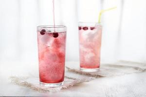 Two glasses of cold pink lemonade with blackcurrant berries on a white background in a blur. photo