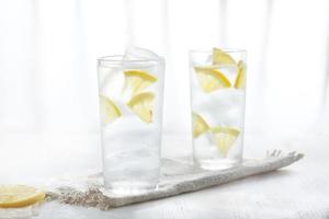 Two glasses of ice cold lemonade with lemon slices on linen napkin on white background in blur.