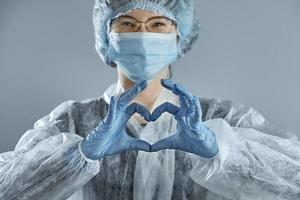 Young woman in glasses with a medical mask and hands in latex glove shows the symbol of the heart. photo