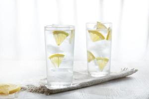 Two glasses of ice cold lemonade on linen napkin on white background in blur. photo