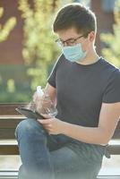 A guy with glasses and a medical mask treated tablet with a sanitizer. photo