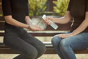 Women's hands are treated with a sanitizer girl's hands against the background of a bench. Outdoor photo. photo