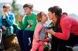 Mother with four kids resting in mountains. Travel and hiking with childrens. Drinking tea in nature. Mommy kiss her daughter.
