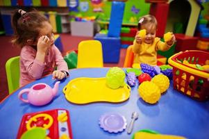 Cute sisters playing in indoor play center. Kindergarten or preschool play room. In the children's kitchen. photo