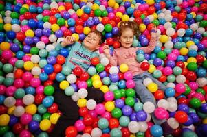 Brother with sister playing in colorful ball pit. Day care indoor playground. Balls pool for children. Kindergarten or preschool play room. photo