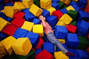 Cute baby girl lying on pool with colored foam cubes in indoor play center. photo