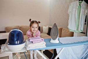 niña como pequeña ayudante de planchado en casa. foto