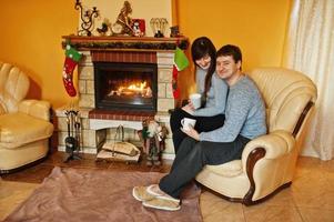 Happy young couple at home by a fireplace in warm living room on winter day. photo