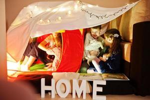 Playing kids with kitty in tent at night home. Hygge mood. photo