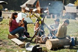 Family bonfire in mountain. Frying sausages. Mother with four kids camping. Autumn hike and camp weather. Warming and cooking near flame together. photo