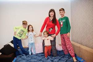 la gran familia feliz se está divirtiendo juntos en el dormitorio. gran concepto de mañana familiar. madre con cuatro hijos usa pijama en la cama en casa. foto