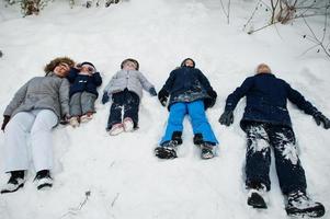 Mother with four children in winter nature lying in the snow.