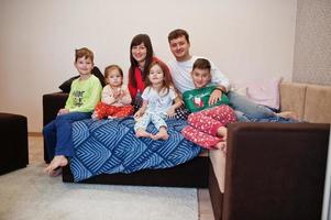 la gran familia feliz se está divirtiendo juntos en el dormitorio. gran concepto de mañana familiar. cuatro niños con padres usan pijamas en la cama en casa. foto