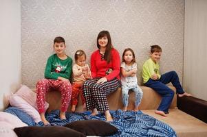 la gran familia feliz se está divirtiendo juntos en el dormitorio. gran concepto de mañana familiar. madre con cuatro hijos usa pijama en la cama en casa. foto