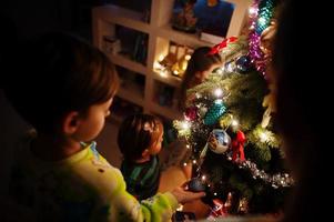 Kids looking on Christmas tree with shining garlands on evening home. photo