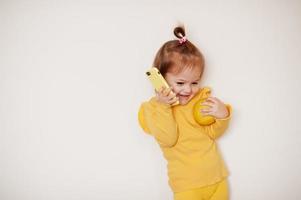 Baby girl in yellow with lemon and mobile phone, isolated background. photo