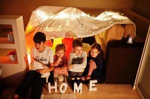 Playing kids with kitty in tent at night home. Hygge mood. photo