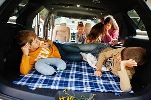 Mother with four kids at vehicle interior. Children in trunk. Traveling by car, lying and having fun, atmosphere concept. photo