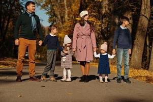 gran familia con cuatro niños tomados de la mano y de pie en la carretera en el parque de otoño. foto