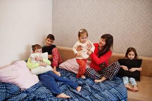 Happy big family is having fun together in bedroom. Large family morning concept. Mother with four kids wear pajamas in bed at home. photo