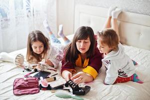 madre e hijas maquillándose en la cama del dormitorio. foto