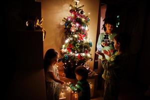 Kids looking on Christmas tree with shining garlands on evening home. photo