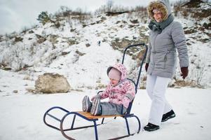 Mother and baby girl enjoy a sleigh ride. Child sledding. Kid riding a sledge on winter. photo