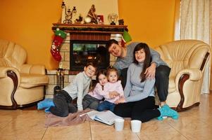 Happy young large family at home by a fireplace in warm living room on winter day. photo