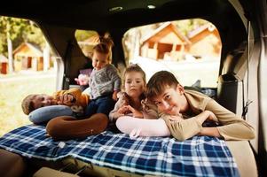 familia de cuatro hijos en el interior del vehículo. niños en el baúl. viajar en coche, mentir y divertirse, concepto de ambiente. foto