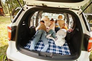 Family of four kids at vehicle interior. Children in trunk. Traveling by car, lying and having fun, atmosphere concept. photo