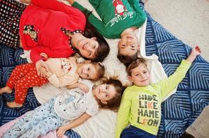 la gran familia feliz se está divirtiendo juntos en el dormitorio. gran concepto de mañana familiar. madre con cuatro hijos usa pijama en la cama en casa. foto