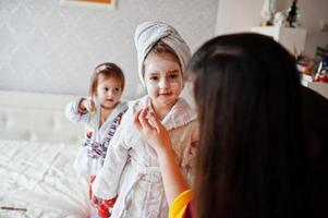 Mother with daughters in a bathrobe with a towel on her head take care of the skin at home, cucumbers on eyes. photo