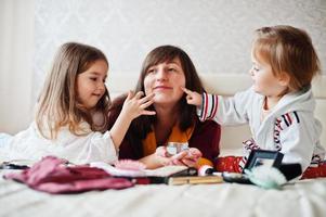 madre e hijas maquillándose en la cama del dormitorio. foto