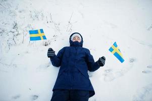 niño escandinavo con bandera de suecia en el paisaje sueco de invierno. foto