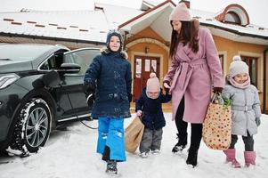 Young woman with kids hold eco bags and charging electric car in the yard of her house . photo