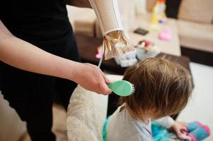 Mom with baby dauhter making everyday routine together. Mother is brushing and drying child hair after shower. photo