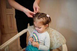 Mother and daughter weekend together at home, mom making hairstyle for baby girl. photo