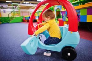 linda niña monta en un coche de plástico en el centro de juegos interior. foto