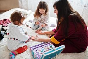 madre e hijas haciendo manicuras en la cama del dormitorio. foto