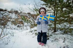 Scandinavian baby girl with Sweden flag in winter swedish landscape. photo