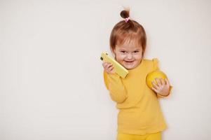 Baby girl in yellow with lemon and mobile phone, isolated background. photo