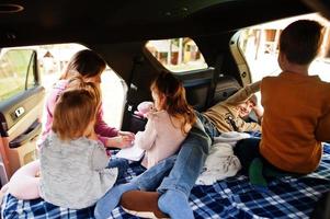 Mother with four kids at vehicle interior. Children in trunk. Traveling by car, lying and having fun, atmosphere concept. photo