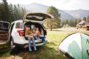 familia de cuatro hijos en el interior del vehículo. niños sentados en el baúl. viajar en coche por las montañas, concepto de ambiente. foto