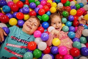 Brother with sister playing in colorful ball pit. Day care indoor playground. Balls pool for children. Kindergarten or preschool play room. photo